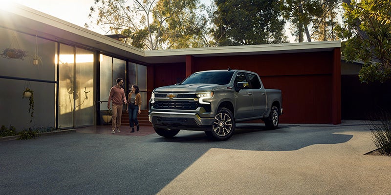 Front side view of the 2025 Chevrolet Silverado parked outside a home, there is a couple standing near the vehicle.