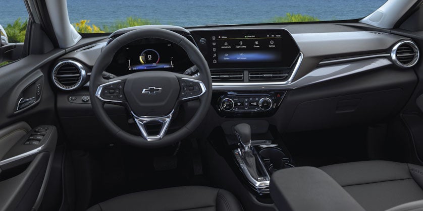 View of the 2025 Chevy Trax's front dashboard from the front passengers point of view. Steering wheel, temperature controls, and touch screen are visible.