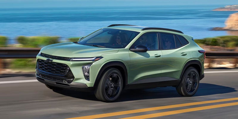 Side view of the 2025 Chevy Trax driving on a mountain road with a body of water in the background.