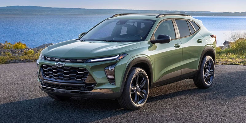Front side view of the 2025 Chevy Trax parked on a grassy hill near some trees.